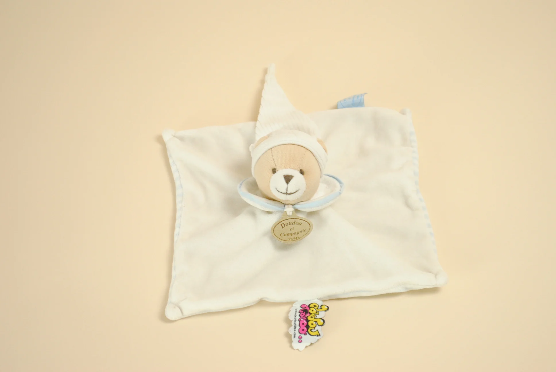 Doudou Ours plat blanc et rayé bleu au verso avec col liseré bleu, bonnet blanc et étiquette Tatoo marque Doudou et Compagnie