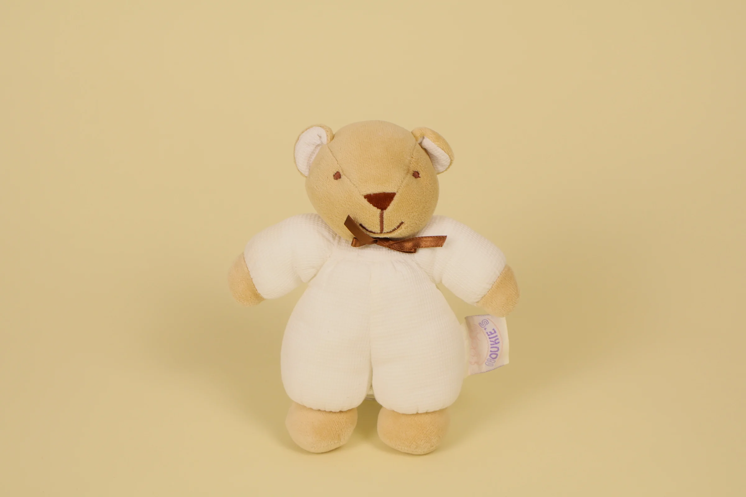 Doudou ours beige et blanc avec nœud marron et grelot sonore marque Noukie's