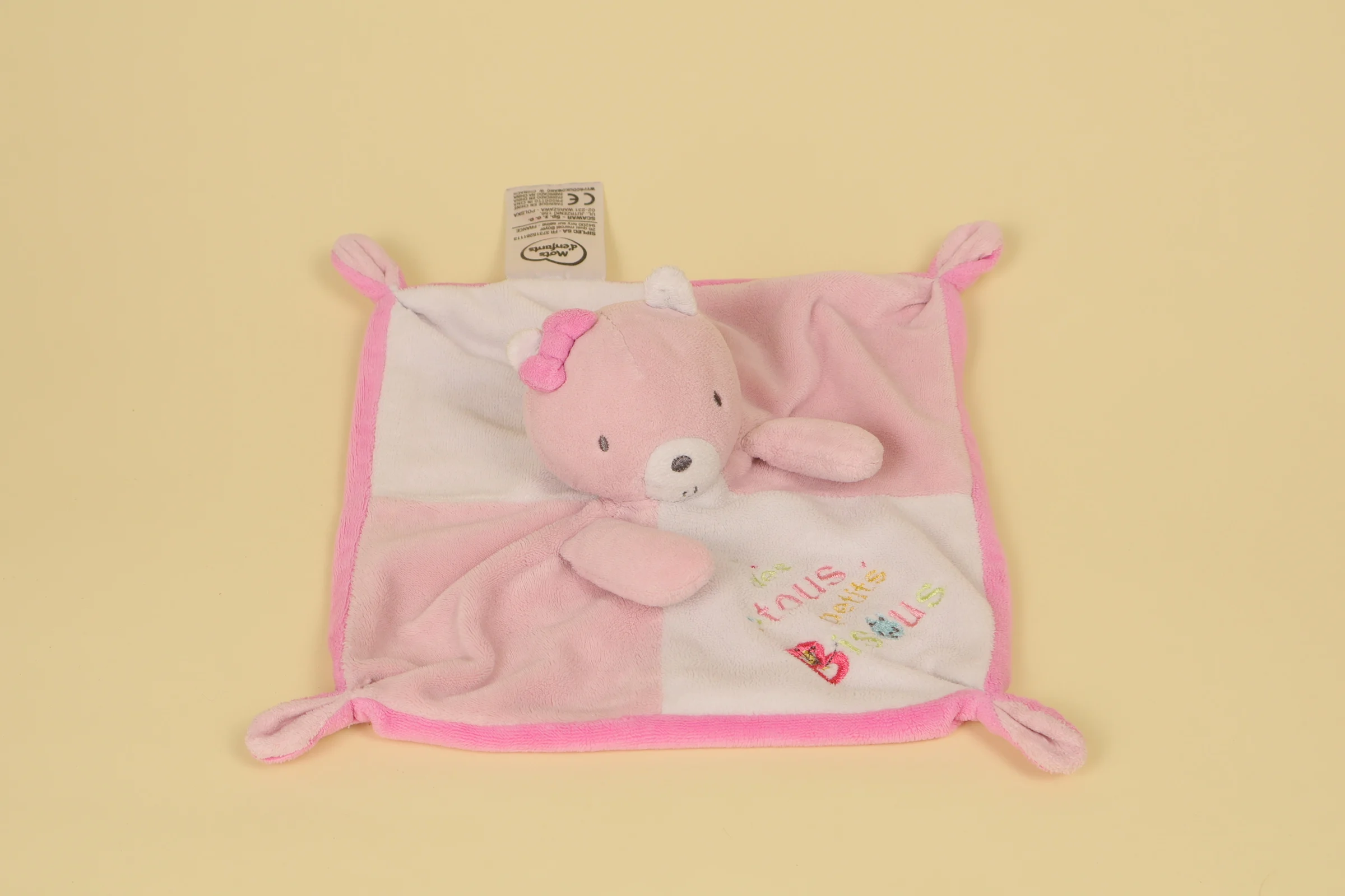 Doudou plat chat blanc et rose de forme mouchoir avec petit nœud sur la tête et inscription brodée Des Tous Petits Bisous marque Mots d'Enfants