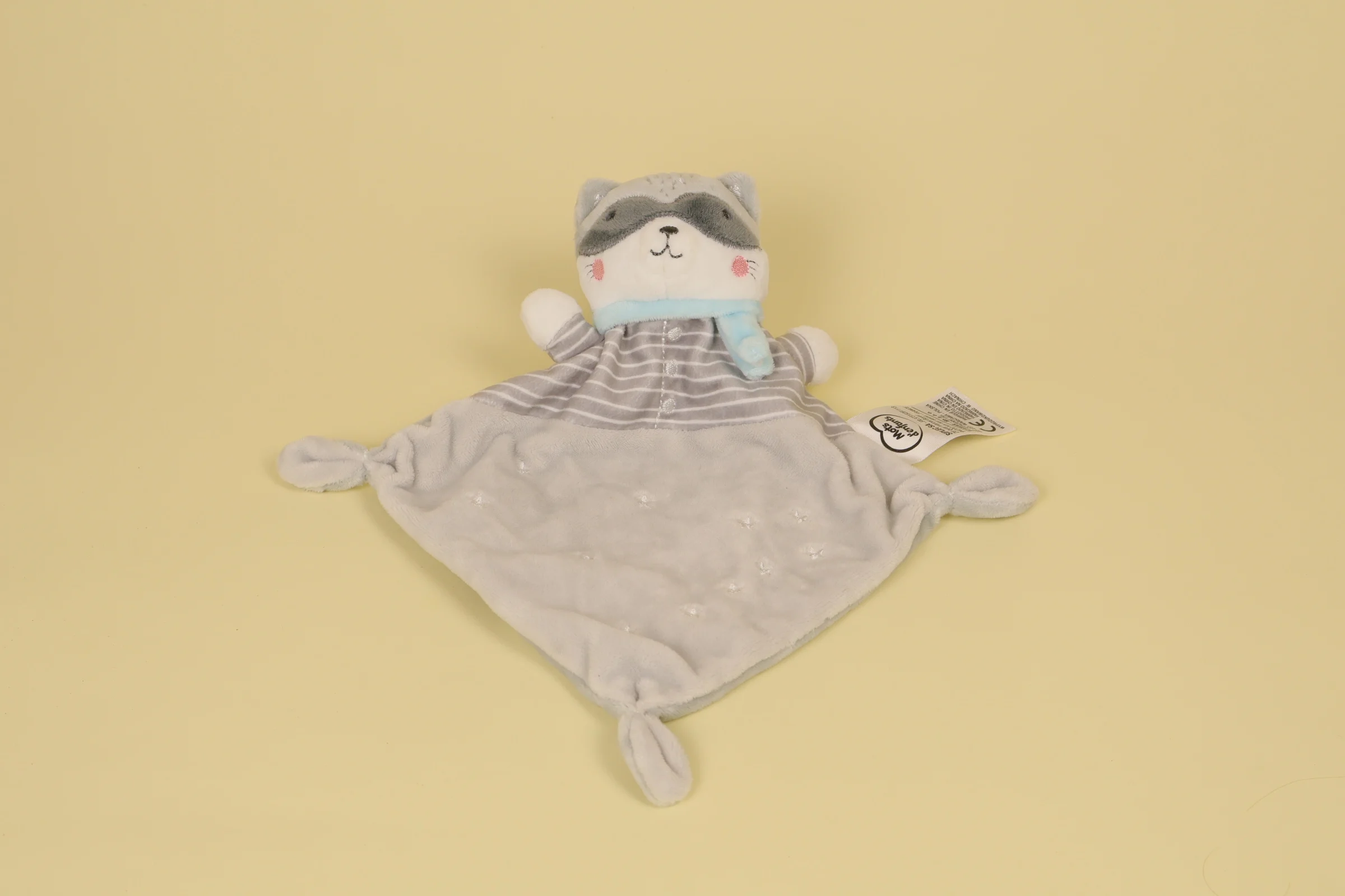 Doudou plat raton laveur gris en forme de losange avec étoiles blanches brodées et petite écharpe bleue autour du cou marque Mots d'Enfants