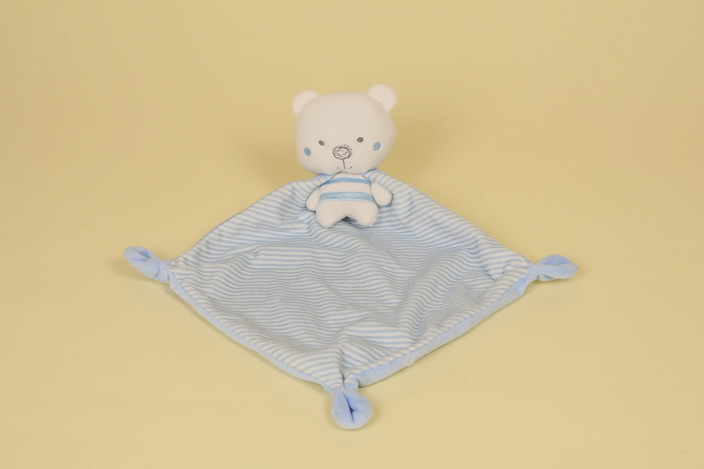 Peluche doudou ours de la marque Mots d'Enfants portant une petite cape de super-héros à rayures bleu et blanc