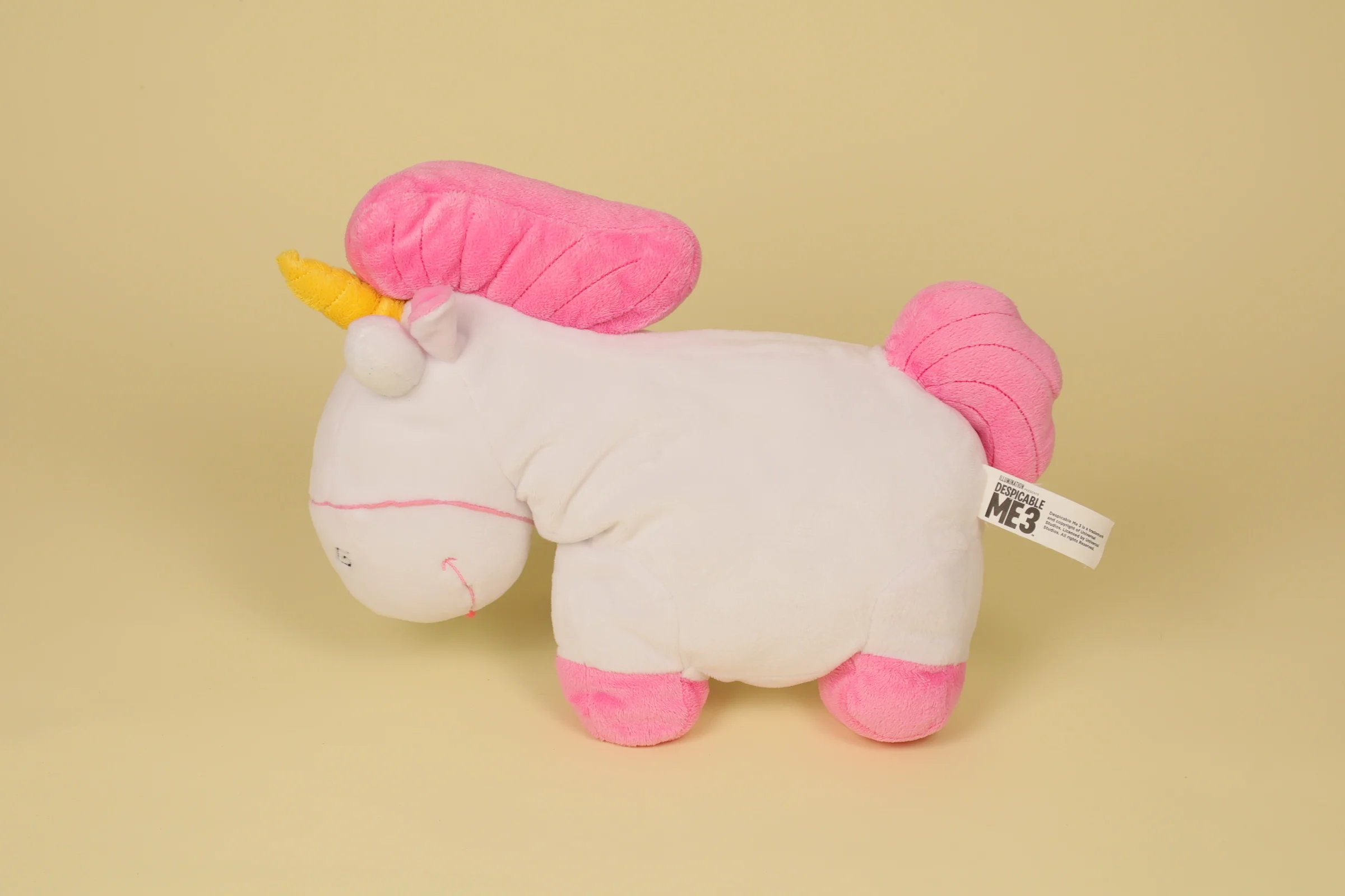 Peluche semi-plat de la licorne Fluffy de la petite Agnes dans Moi Moche et Méchant mesurant 32 cm de long avec sa crinière rose et sa corne dorée marque Universal Studios" profil