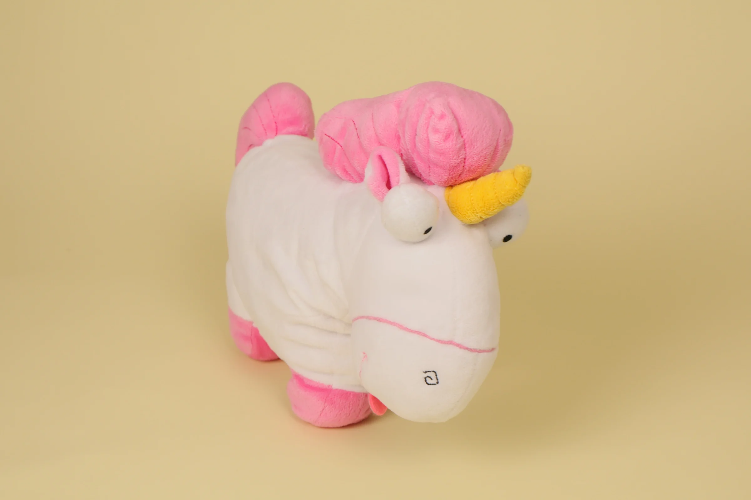 Peluche semi-plat de la licorne Fluffy de la petite Agnes dans Moi Moche et Méchant mesurant 32 cm de long avec sa crinière rose et sa corne dorée marque Universal Studios"