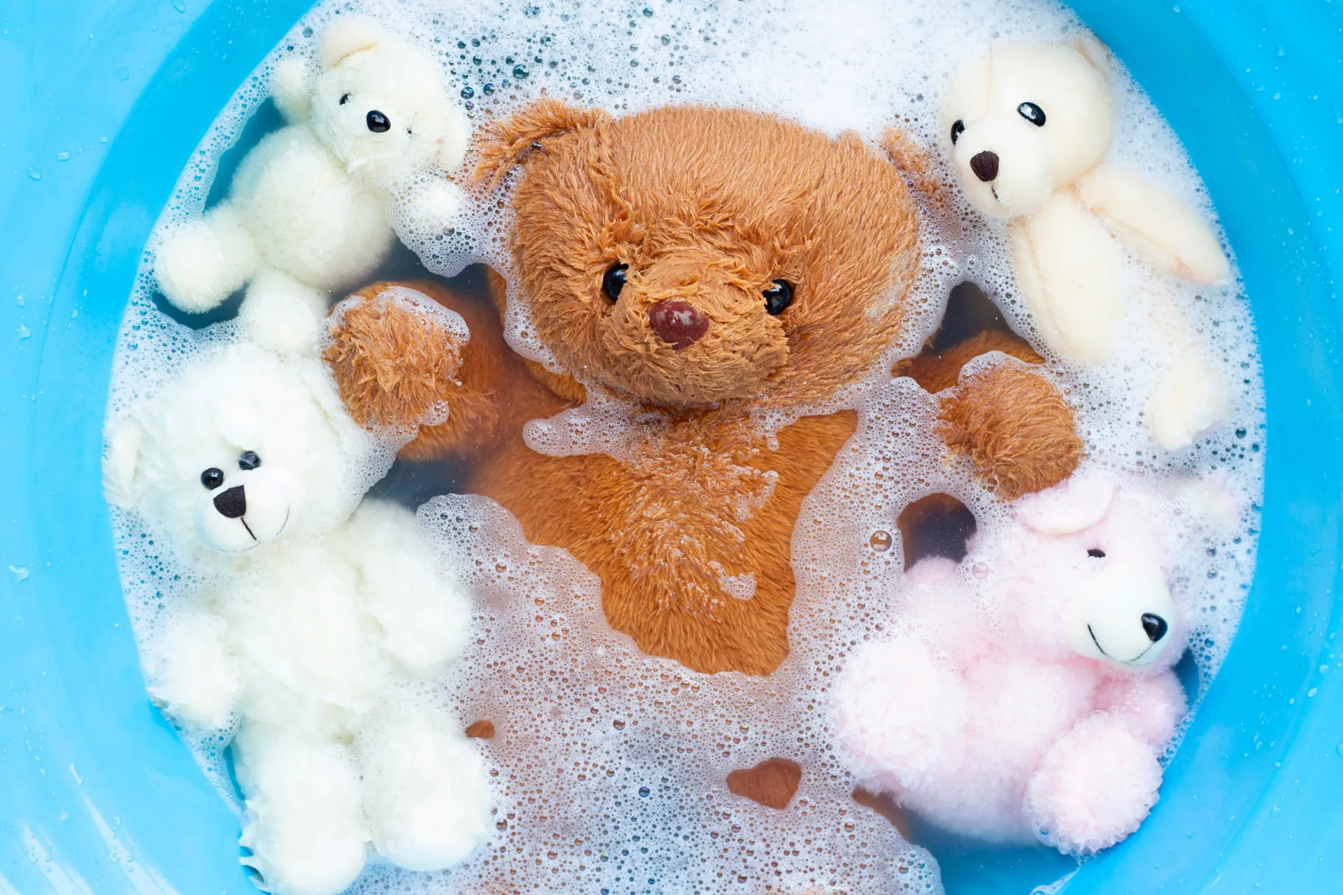 Doudous et ours en peluche dans une bassine d'eau savonneuse pour un lavage délicat