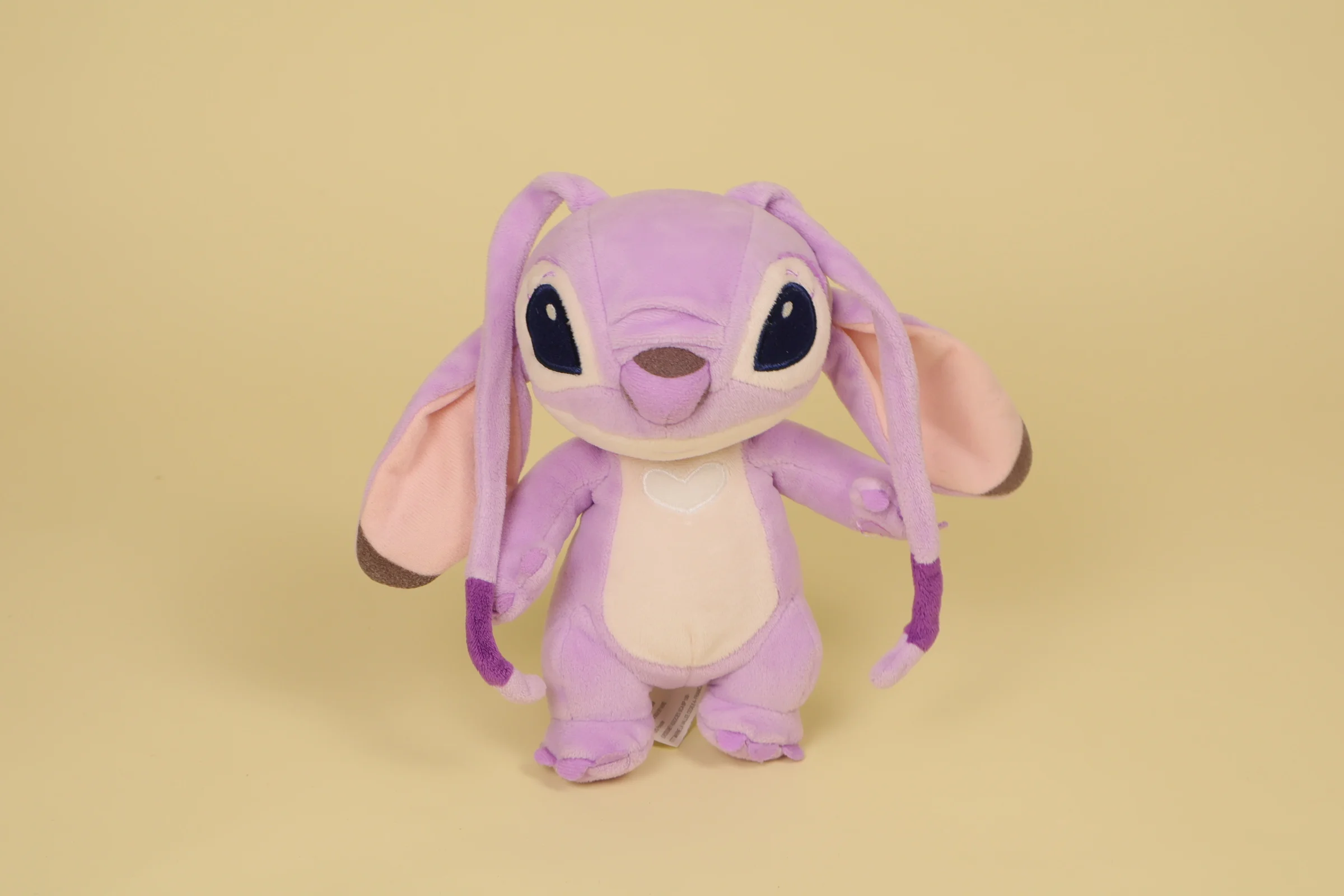 Peluche Angel rose et violet clair debout avec petit cœur blanc brodé sur le ventre mesurant 21 cm de la marque Disneyland Paris