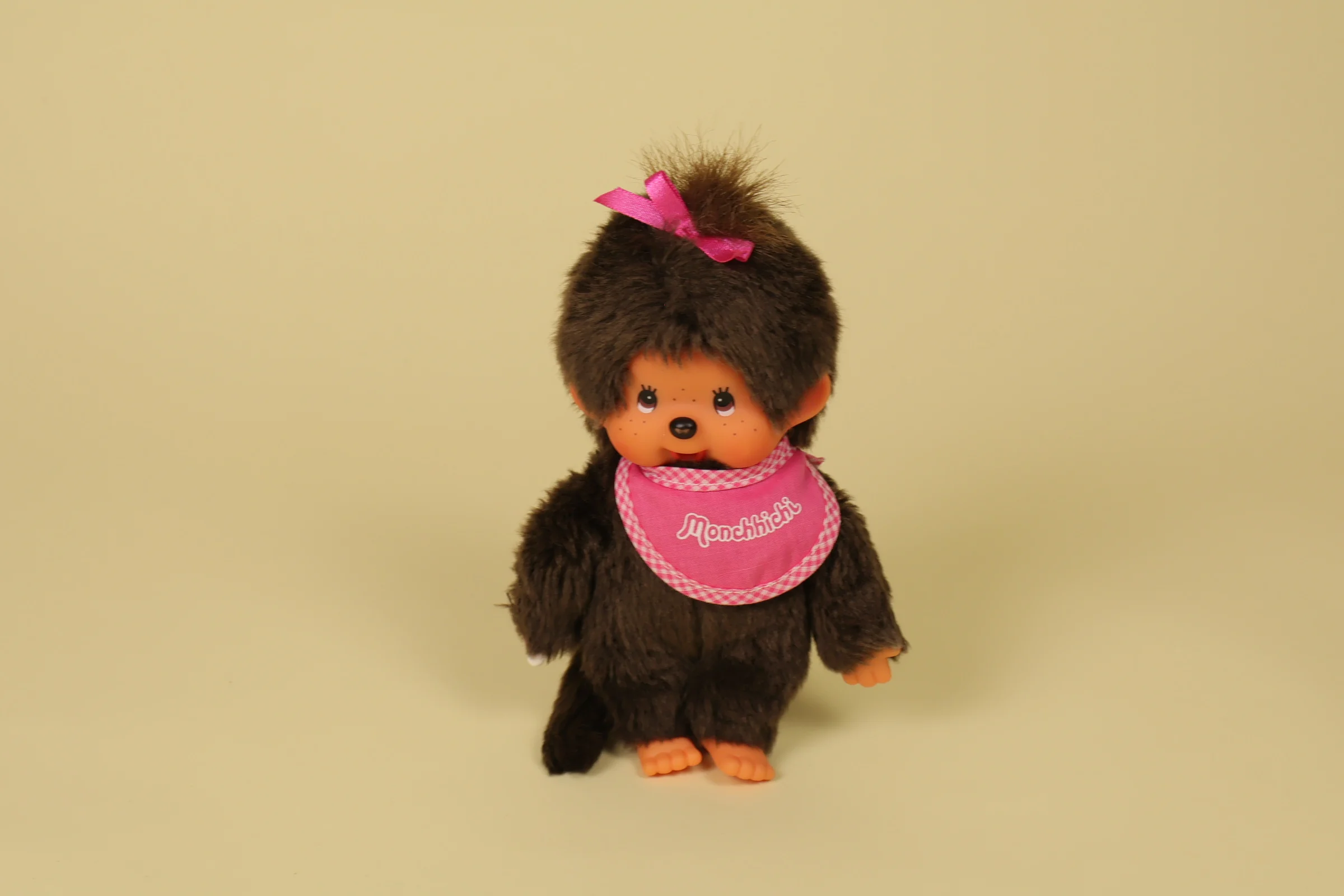 Peluche Kiki Monchhichi de 19 cm avec bavoir et nœud rose de la marque Sekiguchi